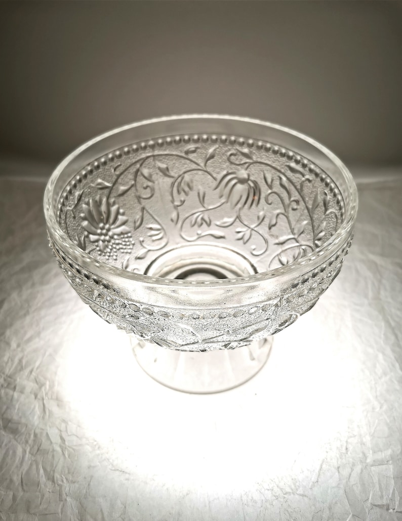 May include: A clear glass bowl with an intricate floral design. The bowl has a pedestal base and is perfect for serving snacks or desserts.