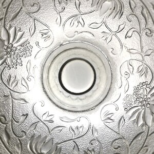 May include: A clear glass bowl with an intricate floral design etched into the bottom. The bowl has a smooth, rounded rim and a slightly raised center.