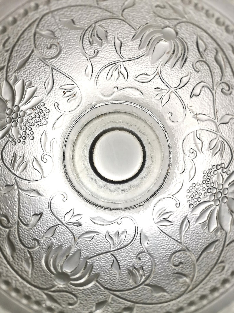 May include: A clear glass bowl with an intricate floral design etched into the bottom. The bowl has a smooth, rounded rim and a slightly raised center.