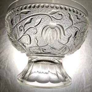 May include: A clear glass bowl with a pedestal base. The bowl has a floral design etched into the glass.