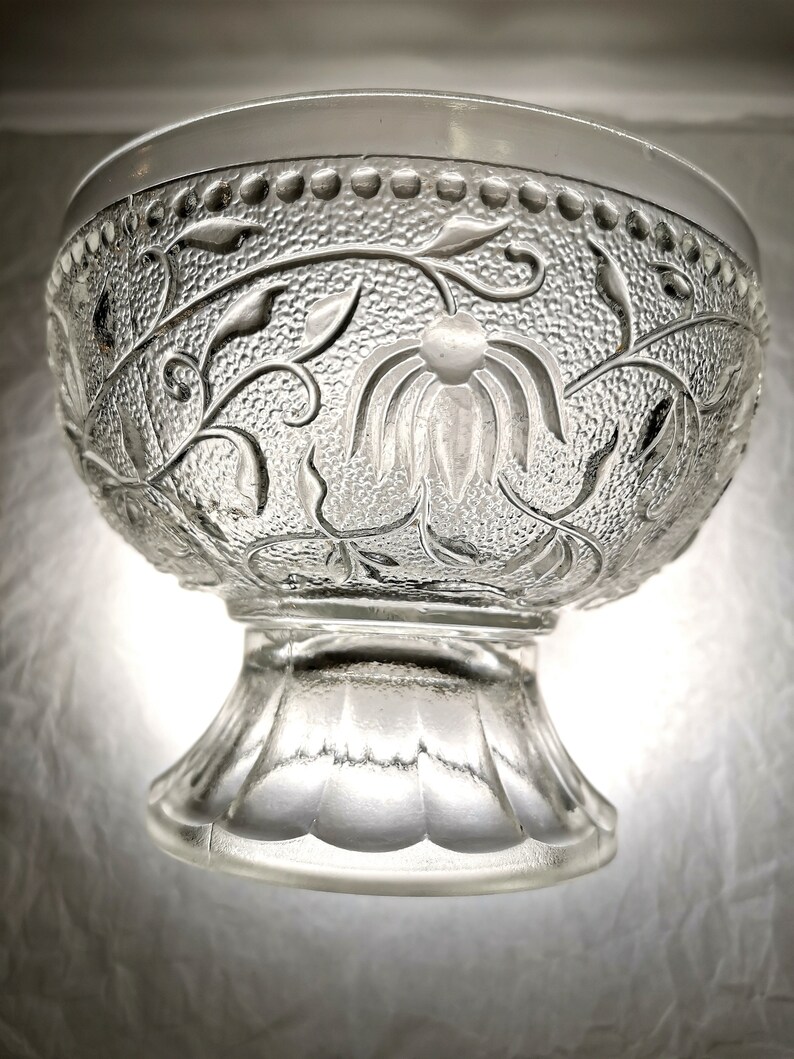 May include: A clear glass bowl with a pedestal base. The bowl has a floral design etched into the glass.