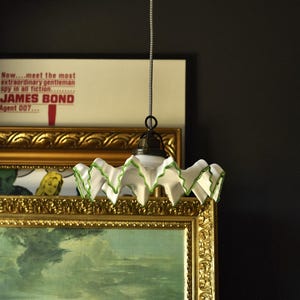 Pode incluir: Uma luminária pendente vintage com babados brancos e verdes. A luz pende de um cabo listrado em preto e branco. O texto "JAMES BOND Agent 007..." é visível no fundo.