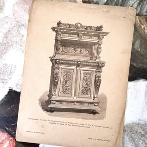 May include: An aged, sepia-toned print of a detailed antique cabinet. The cabinet illustration features ornate carvings, two doors with portrait medallions, and a decorative top. Text in German is visible at the bottom of the print.