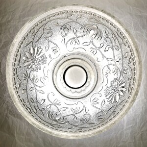 May include: A clear glass bowl with a floral design etched into the surface. The bowl has a raised center section and a scalloped edge.