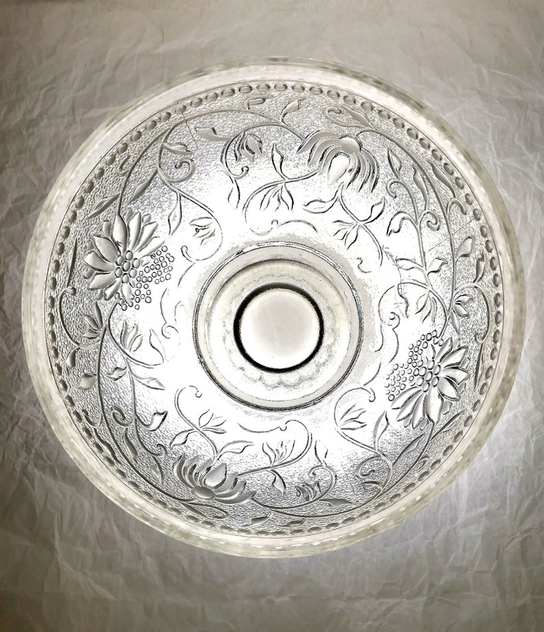 May include: A clear glass bowl with a floral design etched into the surface. The bowl has a raised center section and a scalloped edge.