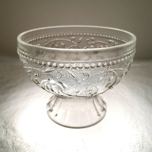 May include: A clear glass bowl with a pedestal base and an intricate floral design.