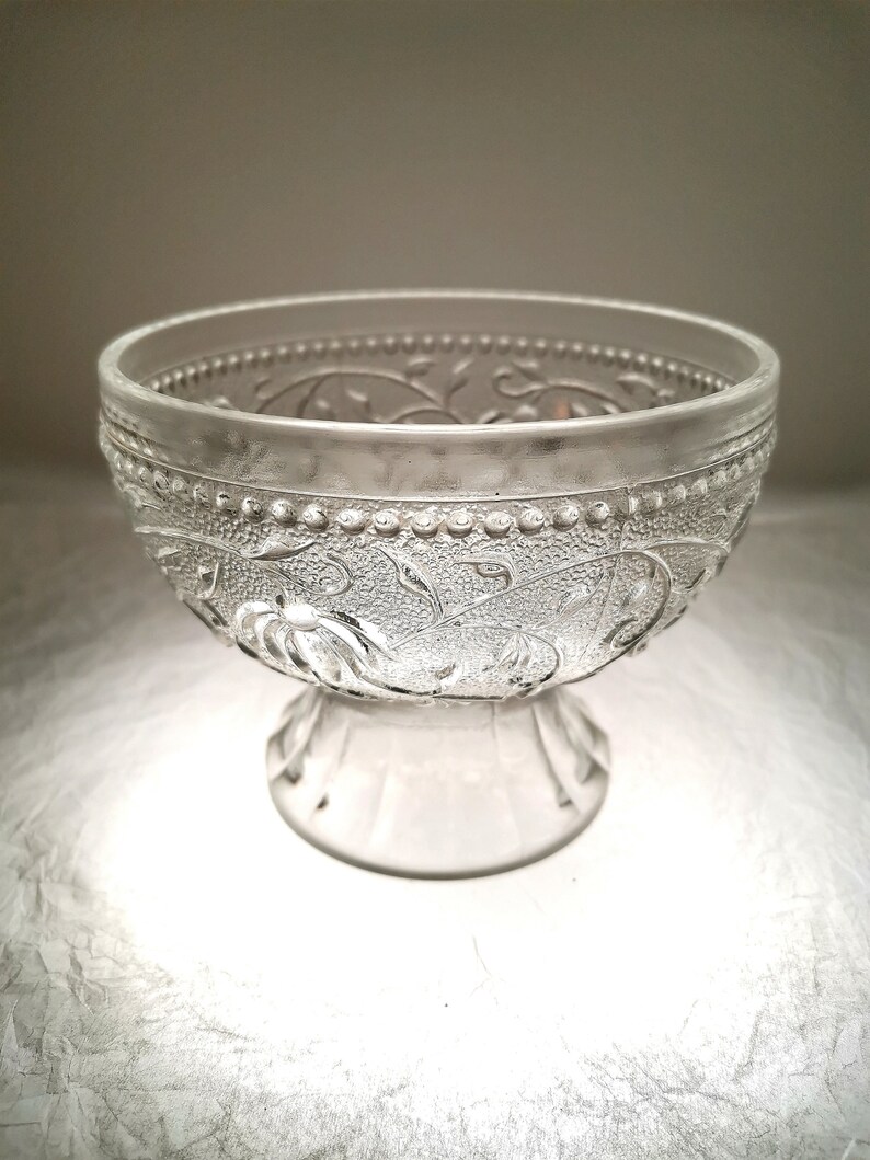 May include: A clear glass bowl with a pedestal base and an intricate floral design.
