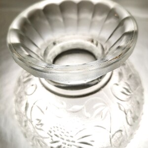 May include: A clear glass bowl with a decorative floral pattern. The bowl has a raised center section with a scalloped edge.