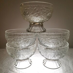 May include: Set of five clear glass bowls with a floral design. The bowls are stacked on top of each other, with the largest bowl on the bottom and the smallest bowl on top.