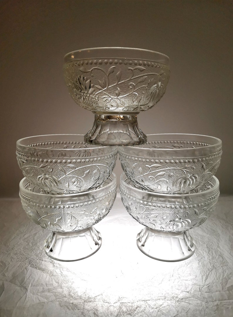May include: Set of five clear glass bowls with a floral design. The bowls are stacked on top of each other, with the largest bowl on the bottom and the smallest bowl on top.