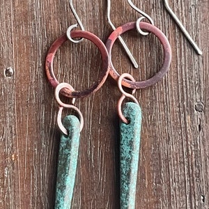 Puede incluir: Un par de pendientes de cobre y turquesa con acabado martillado. Los pendientes tienen un pequeño aro de cobre con un colgante turquesa.