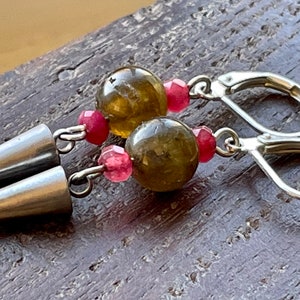 May include: A pair of silver earrings with green and pink gemstone beads. The earrings have a silver cone-shaped dangle and a silver hoop.