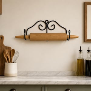May include: A wooden rolling pin with a black metal holder mounted on a wall. The rolling pin is light brown, and the holder has decorative swirls. Kitchen utensils and a cutting board are also visible.