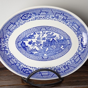 May include: A white oval serving platter with a blue and white willow pattern. The pattern features a traditional Chinese landscape with trees, houses, and a bridge.