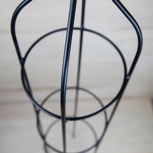 May include: Black metal plant stand with three tiers. The stand is designed to support climbing plants.