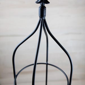 May include: Black metal plant stand with a pointed finial on top. The stand has three tiers.