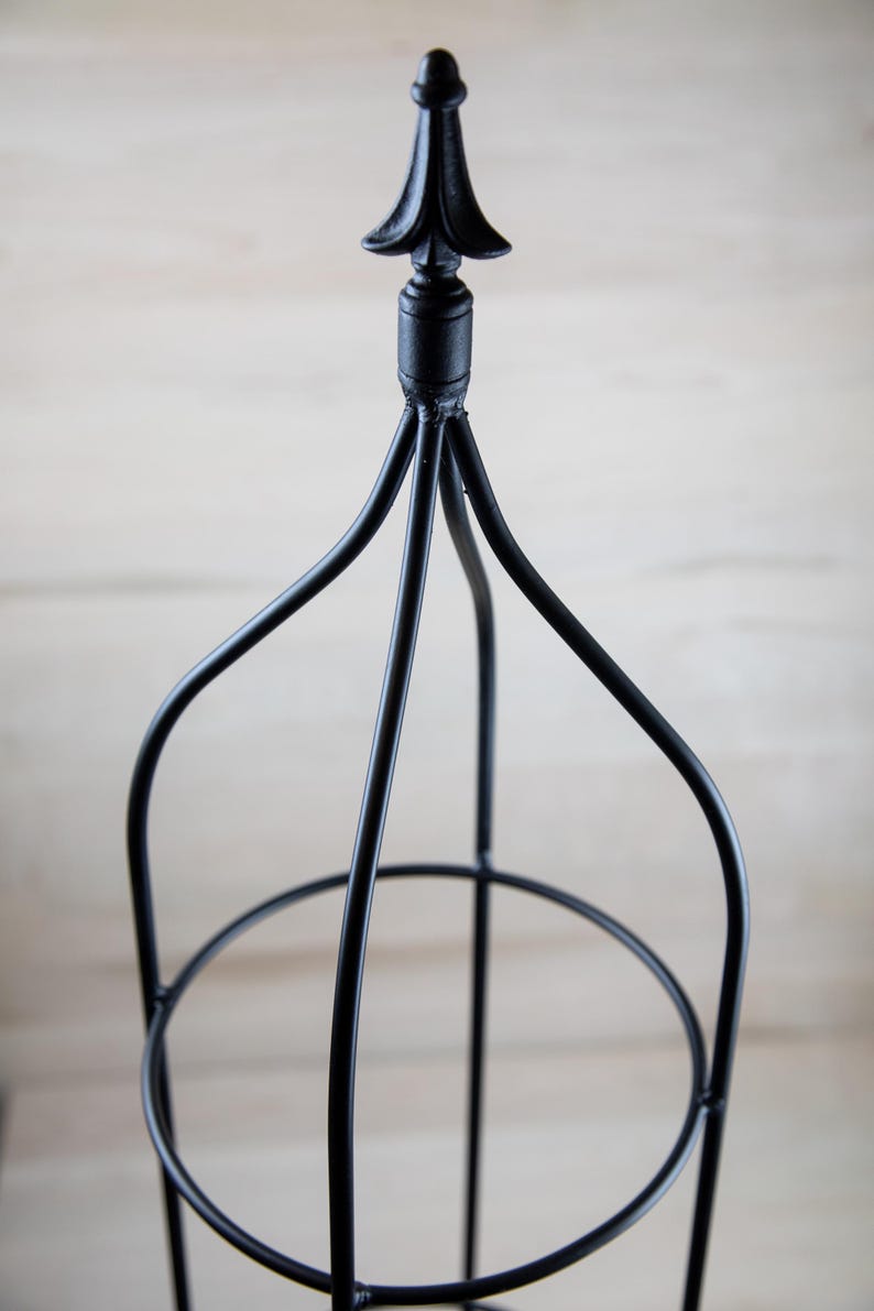 May include: Black metal plant stand with a pointed finial on top. The stand has three tiers.