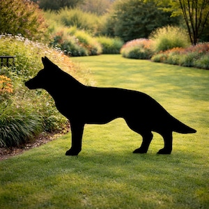 May include: A black silhouette of a dog, likely a German Shepherd, standing on a grassy lawn. The dog is facing left, with its ears perked up and tail extended. The background features a garden with green grass, bushes, and trees.