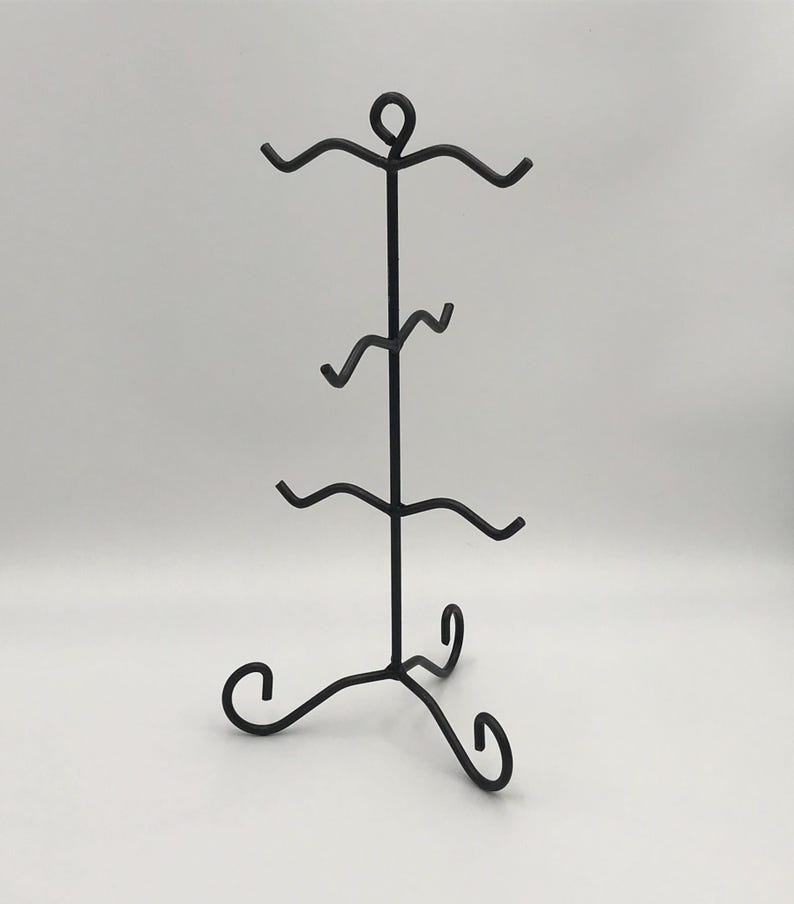 May include: A black metal jewellery display stand with a three-legged base and a vertical post. The post has four curved arms to hold items. The top of the stand has a circular design. The stand is designed to hold jewellery.