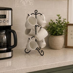 May include: A kitchen setting with a coffee machine, a black mug tree with white mugs, and a framed sign saying "COFFEE IS ALWAYS A GOOD IDEA." A small potted plant is also visible. The time on the coffee machine is 10:30.