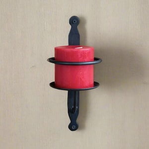 May include: Black metal candle holder with a red candle. The holder has a simple design with a round base and a vertical bar.