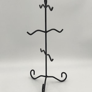 May include: Black metal display stand with a three-tiered design. The stand has decorative scrollwork at the base and top, with curved arms to hold items. Suitable for displaying jewellery, small art, or collectibles.
