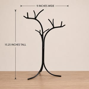 May include: A black metal tree-shaped decorative stand, 15.25 inches tall and 9 inches wide. The stand has a curved base and branches extending upwards. The stand is on a wooden surface.