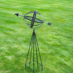 May include: A black metal garden ornament with a sphere and arrow design. The sphere is made of metal rods and is mounted on a tall, pointed stand.