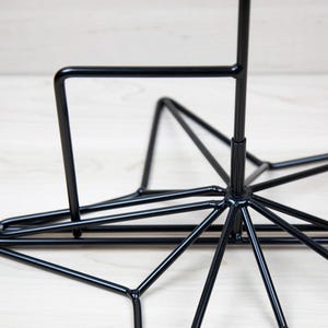 Peut inclure: Un support en métal noir en forme d'étoile avec une tige verticale s'étendant du centre. Le support a un design géométrique avec plusieurs points.