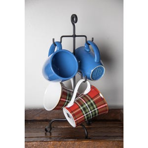 May include: A black metal mug rack with four mugs hanging from it. Two of the mugs are blue and two are red and green plaid.