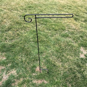 May include: A black metal garden flag stand with a curved arm. The stand is designed to hold a flag or banner.