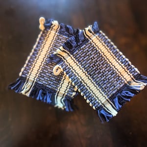 Può includere: Due presine da cucina in tessuto a righe blu e bianche con bordi a frangia.