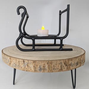 May include: Black metal sleigh candle holder with a white candle on a wooden slice stand with black metal legs.