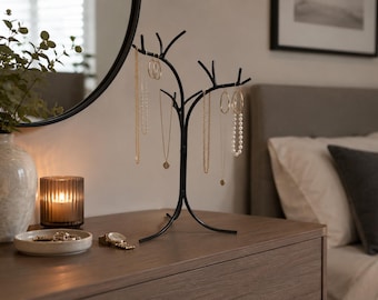 May include: A black metal jewellery stand shaped like a tree with multiple branches for hanging necklaces and earrings. The stand features a curved base and several hooks to organise various gold-toned chains and beaded jewellery pieces.