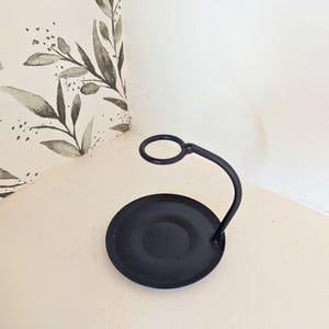 Pode incluir: Castiçal de metal preto com base redonda e um braço curvo com um anel no topo.