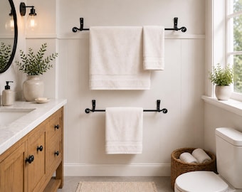 May include: A bathroom interior with black towel rails and white towels. The room includes a wooden vanity unit, a round mirror, and a window with a small plant. A woven basket contains rolled towels. The walls are painted white.