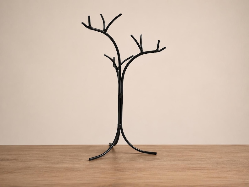 May include: A black metal tree-shaped decorative stand. The stand has a central trunk with multiple branches extending upwards. The base has three curved legs. The stand is on a wooden surface.