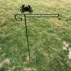 May include: Black metal garden flag stand with a crab silhouette at the top. The stand is designed to hold a flag or banner.