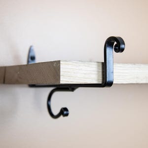 以下が含まれることがあります： 装飾的なスクロールデザインとフックが付いた黒い金属製の棚ブラケット。ブラケットは木製棚に取り付けられています