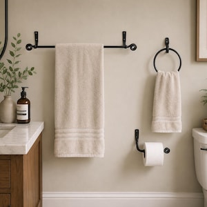 May include: A bathroom set featuring a black towel rack, towel ring, and toilet paper holder. The set includes beige towels. The bathroom also has a wooden vanity, a mirror, and a framed botanical print.