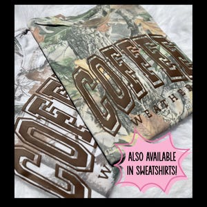 May include: Two camouflage-patterned shirts with the word "GOFFER" in brown block letters. The word "WEATHER" is printed below the main text. One shirt is white and brown, the other is green and brown.