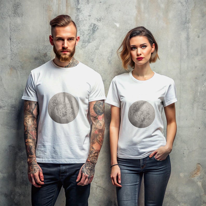 May include: Two people wearing white t-shirts with a gray moon graphic print. The moon graphic is centered on the chest of each shirt.
