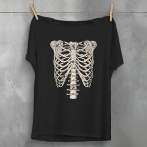 Op de afbeelding: Zwart T-shirt met een witte afbeelding van een ribbenkast met bloemmotieven.