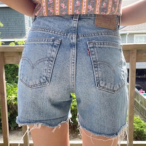 K&ouml;nnte beinhalten: Hellblaue Jeans-Shorts mit ausgefransten Kanten. Die Shorts haben eine hohe Taille und ein klassisches Design mit f&uuml;nf Taschen. Das Levi's-Logo ist auf der Ges&auml;&szlig;tasche sichtbar.