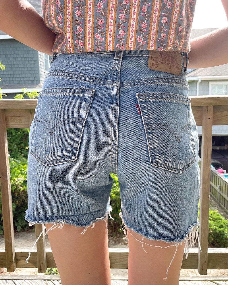 K&ouml;nnte beinhalten: Hellblaue Jeans-Shorts mit ausgefransten Kanten. Die Shorts haben eine hohe Taille und ein klassisches Design mit f&uuml;nf Taschen. Das Levi's-Logo ist auf der Ges&auml;&szlig;tasche sichtbar.