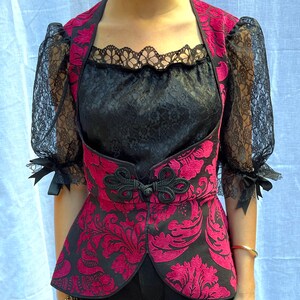 May include: A black and red brocade vest with a lace trim neckline. The vest has a floral pattern and a cinched waist.