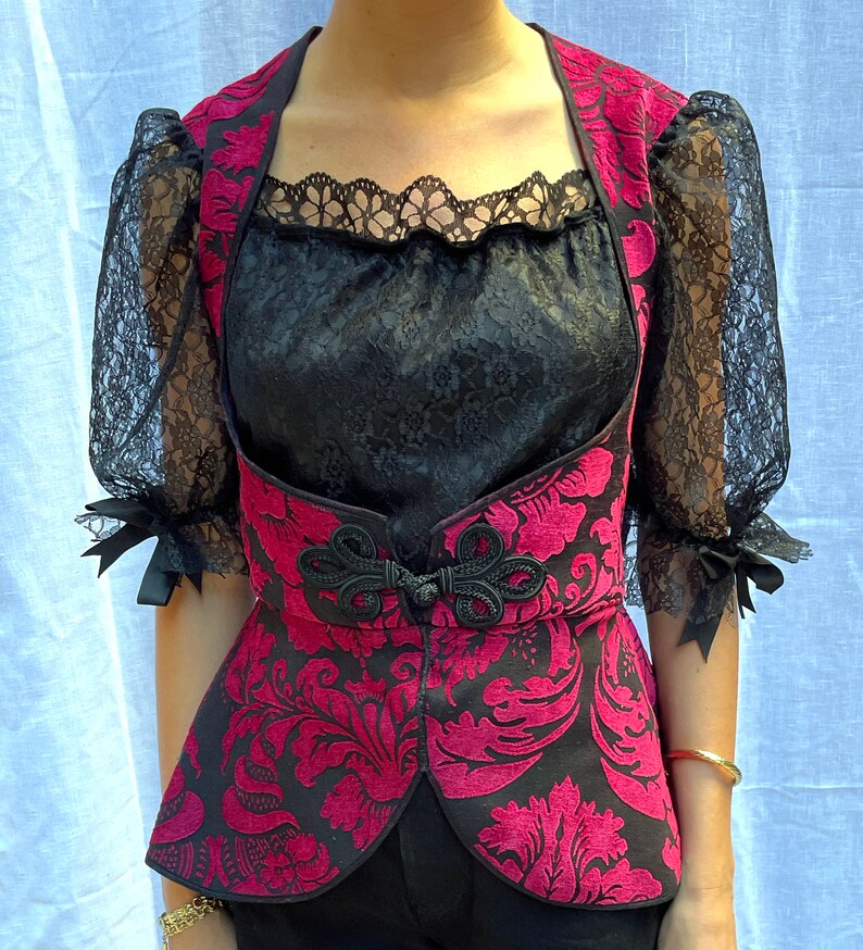 May include: A black and red brocade vest with a lace trim neckline. The vest has a floral pattern and a cinched waist.