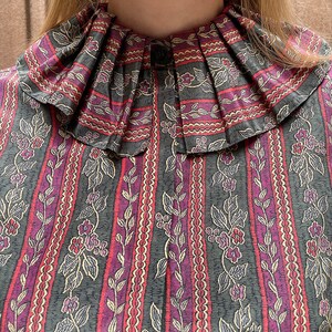 May include: A vintage blouse with a large, pleated collar. The fabric is a dark green with a repeating pattern of pink and white stripes, vines, and small flowers.