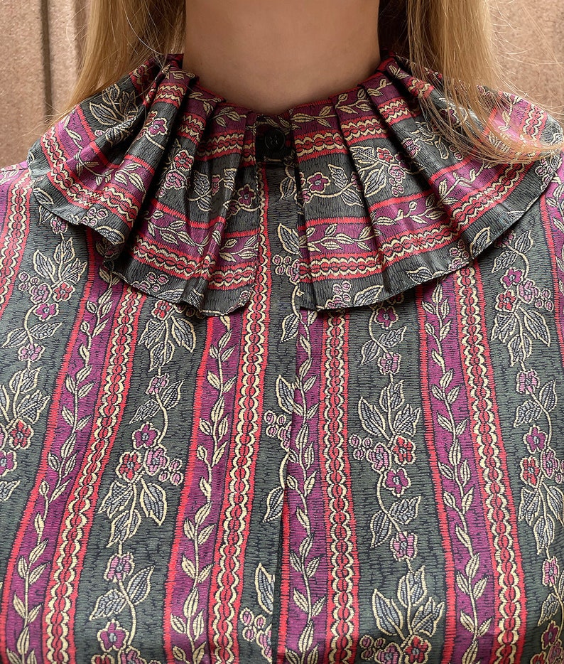 May include: A vintage blouse with a large, pleated collar. The fabric is a dark green with a repeating pattern of pink and white stripes, vines, and small flowers.