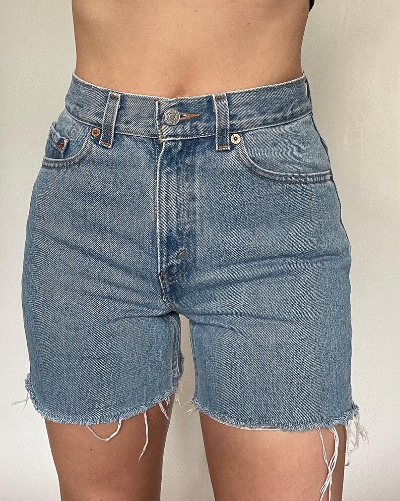 K&ouml;nnte beinhalten: Hellblaue Jeans-Shorts mit ausgefranstem Saum. Die Shorts haben eine hohe Taille und f&uuml;nf Taschen.